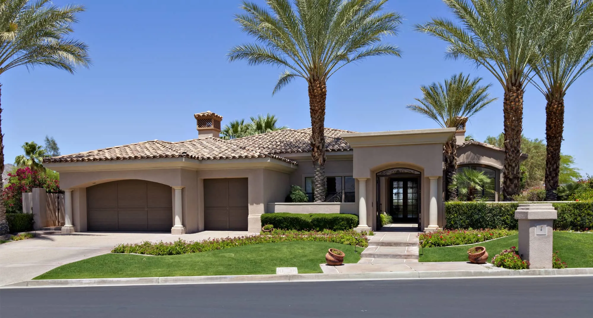Spanish-style home with a tile roof, palm trees and a front lawn